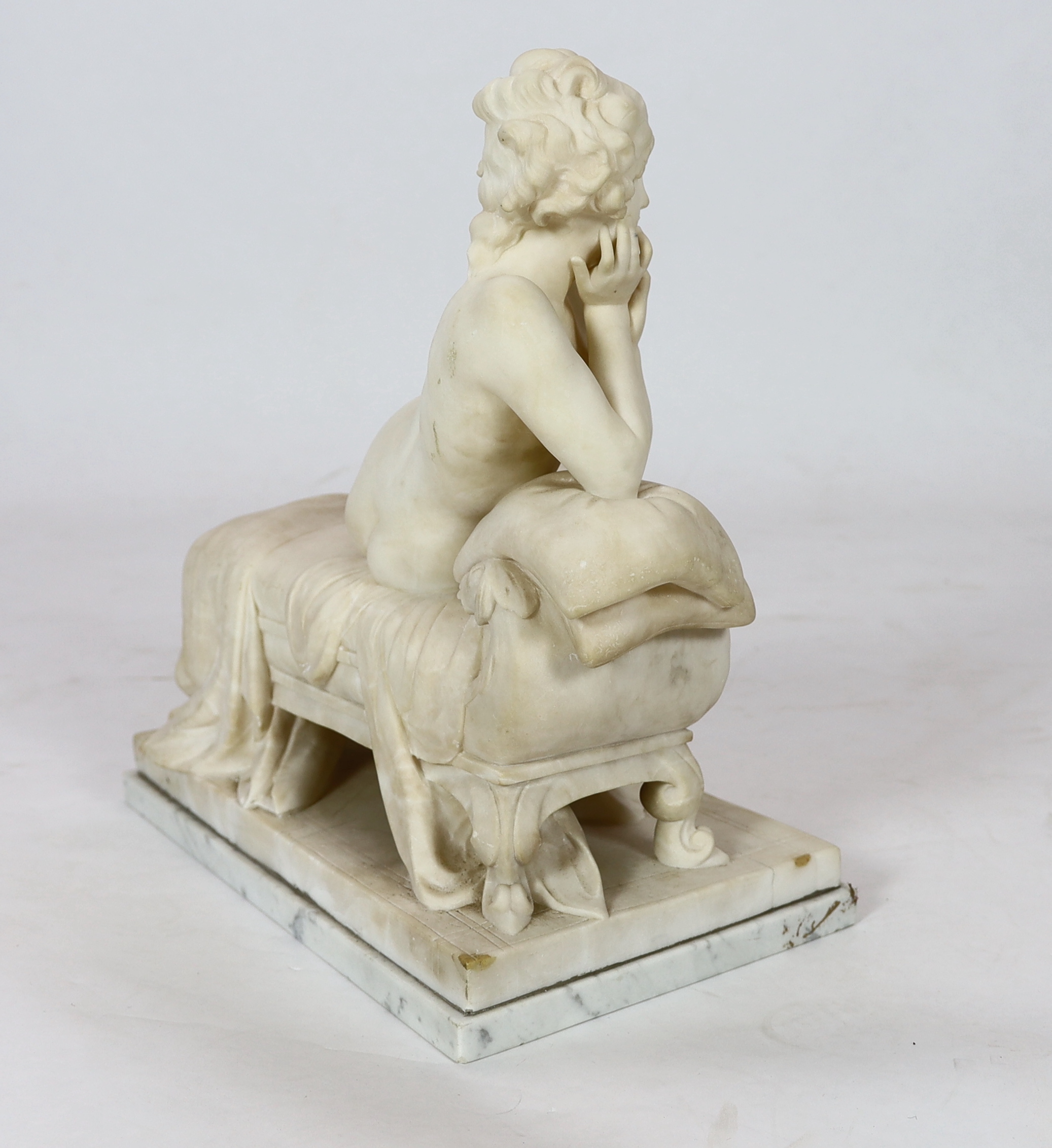 An early 20th century French carved white marble figure of a semi-clad woman seated upon a daybed, 50cm wide, 29cm deep, 52cm high